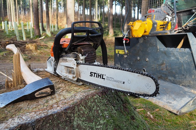 An ax, chainsaw, and bulldozer by a stump in the forest